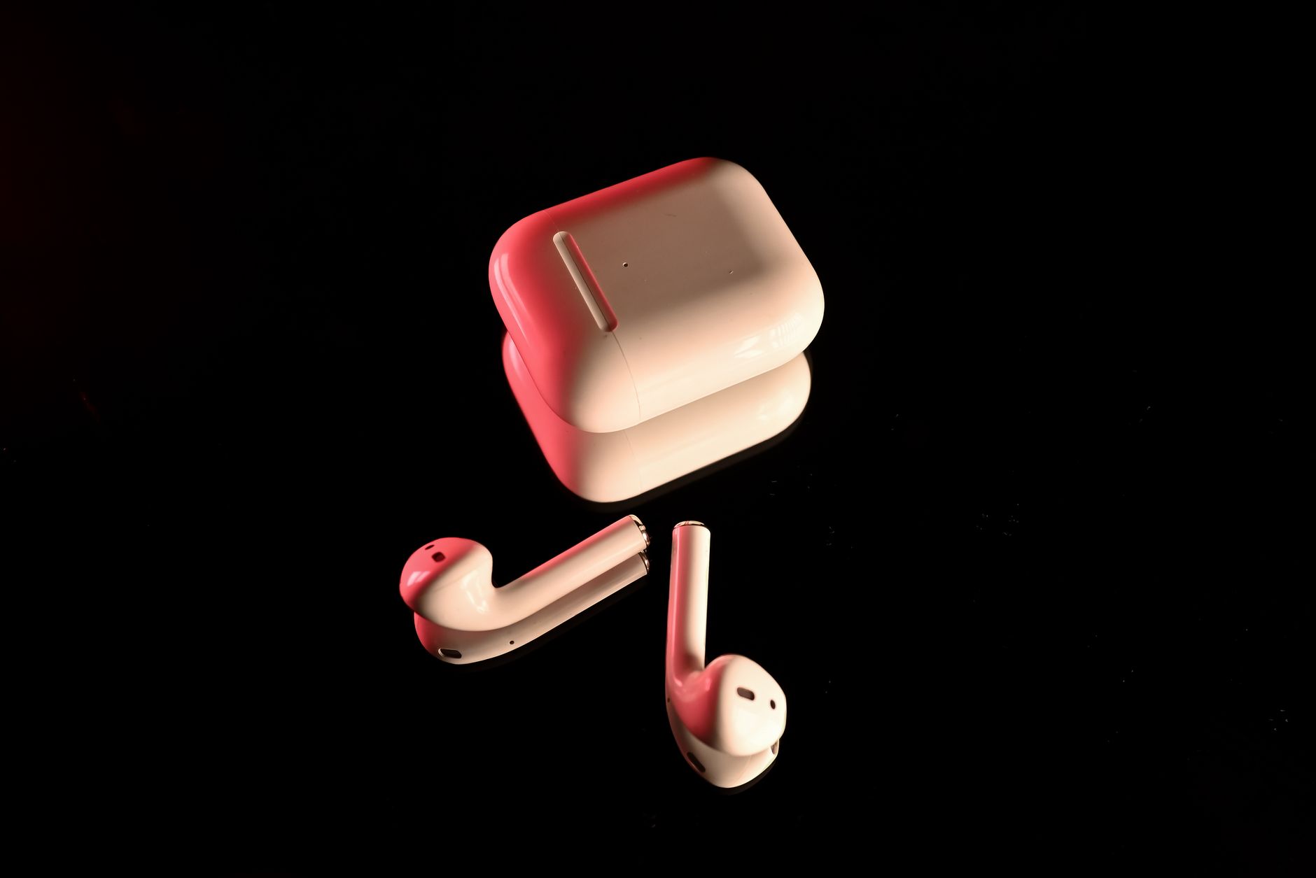 auricolari Anker — White wireless earbuds with a charging case, highlighted with red lighting on a reflective black surface.