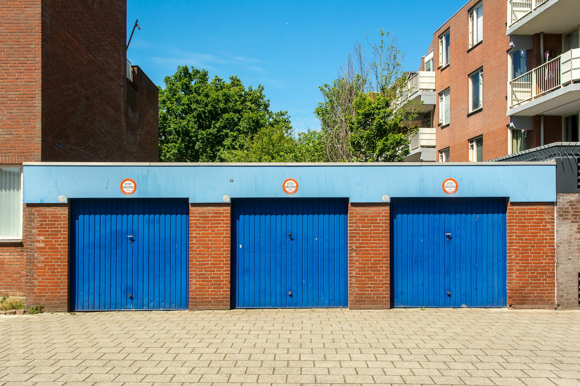 prezzi box auto Roma — Three blue garage doors in a brick building on a sunny day.