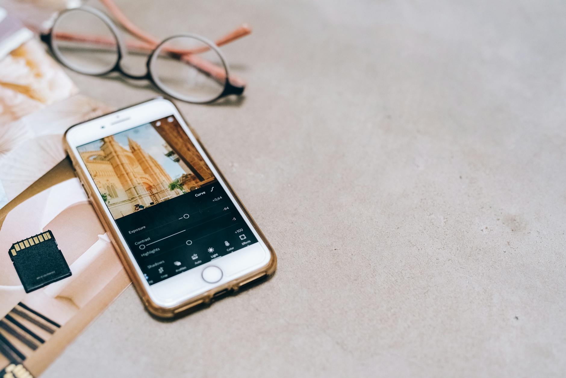 fotografia mobile — Smartphone displaying a photo editing app, next to a memory card and glasses on a table.