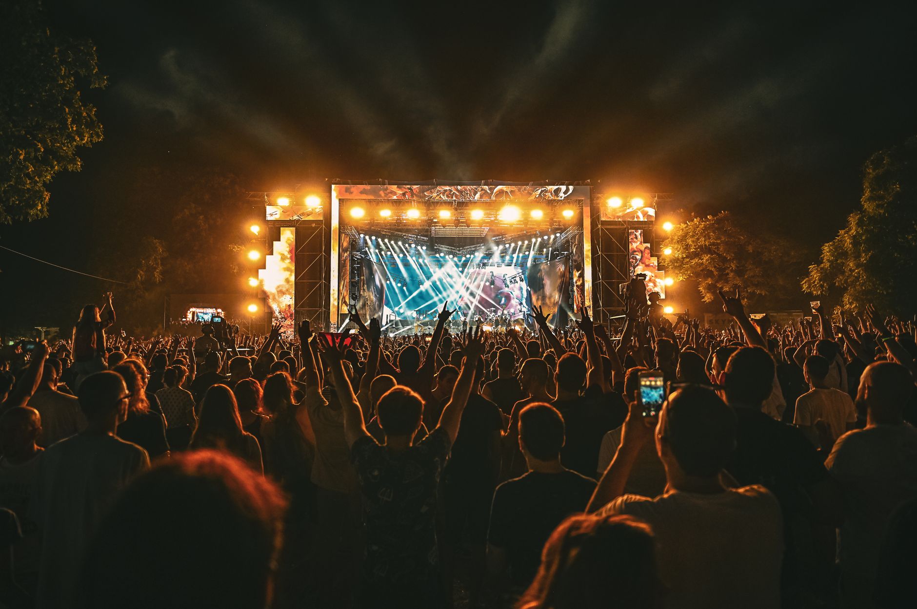programmazione concerti estate 2026 — Large crowd enjoying a spectacular live outdoor concert at night with stage lighting effects.
