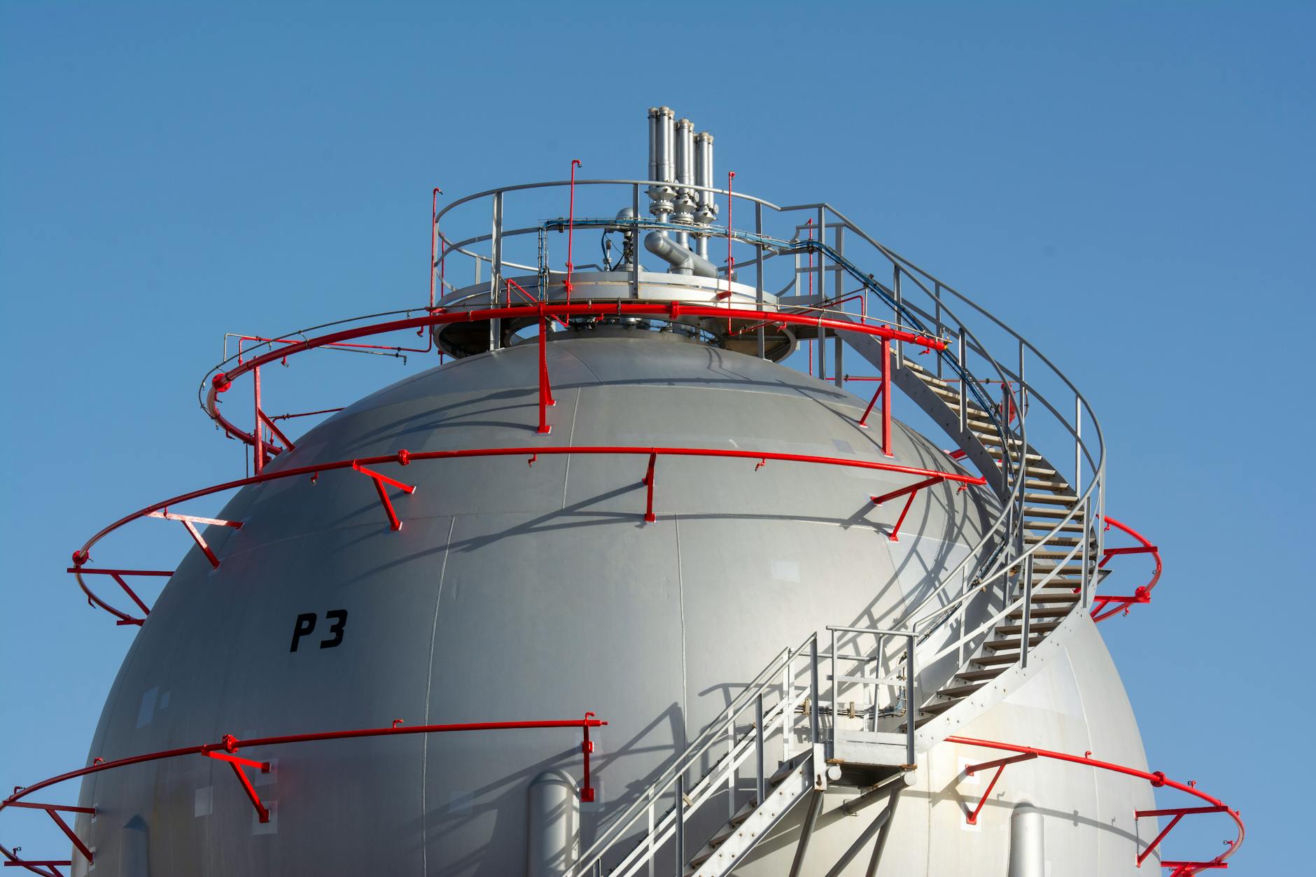 prezzo gas naturale — Close-up view of a large industrial gas storage sphere with a surrounding metal staircase.