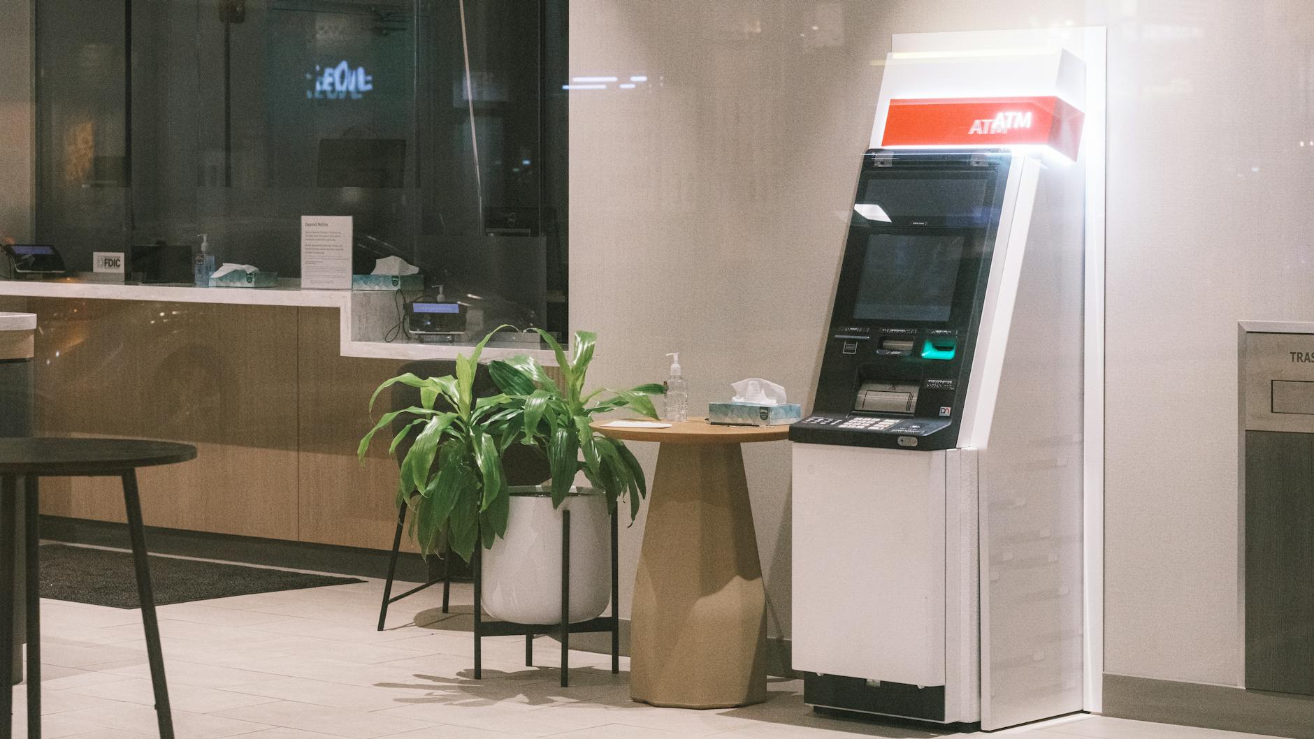 tagli BNP Paribas — An ATM machine stands in a modern bank lobby, next to a plant and table.
