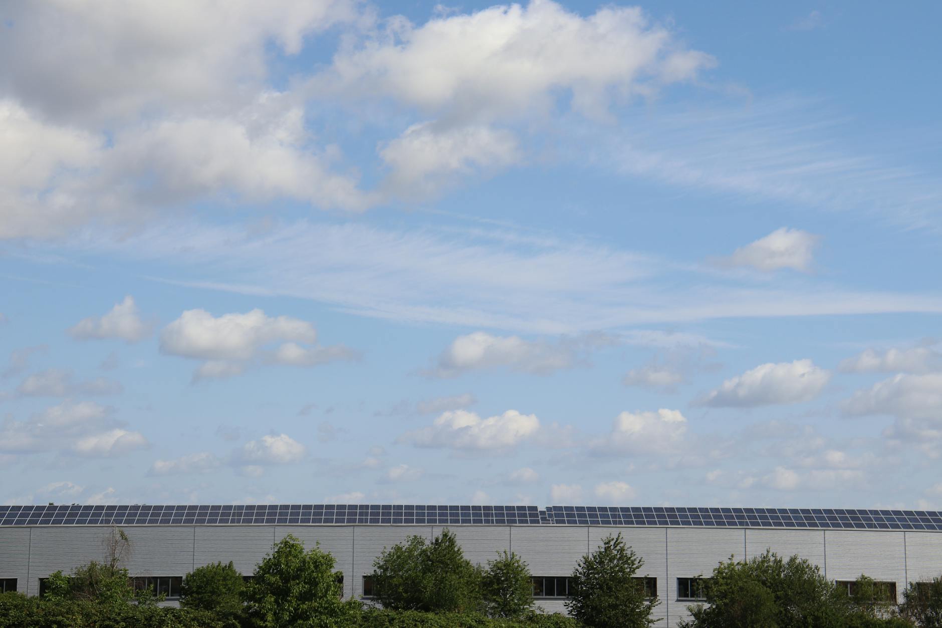 stanziamento record 14 miliardi — Warehouse roof adorned with solar panels beneath a bright blue sky.