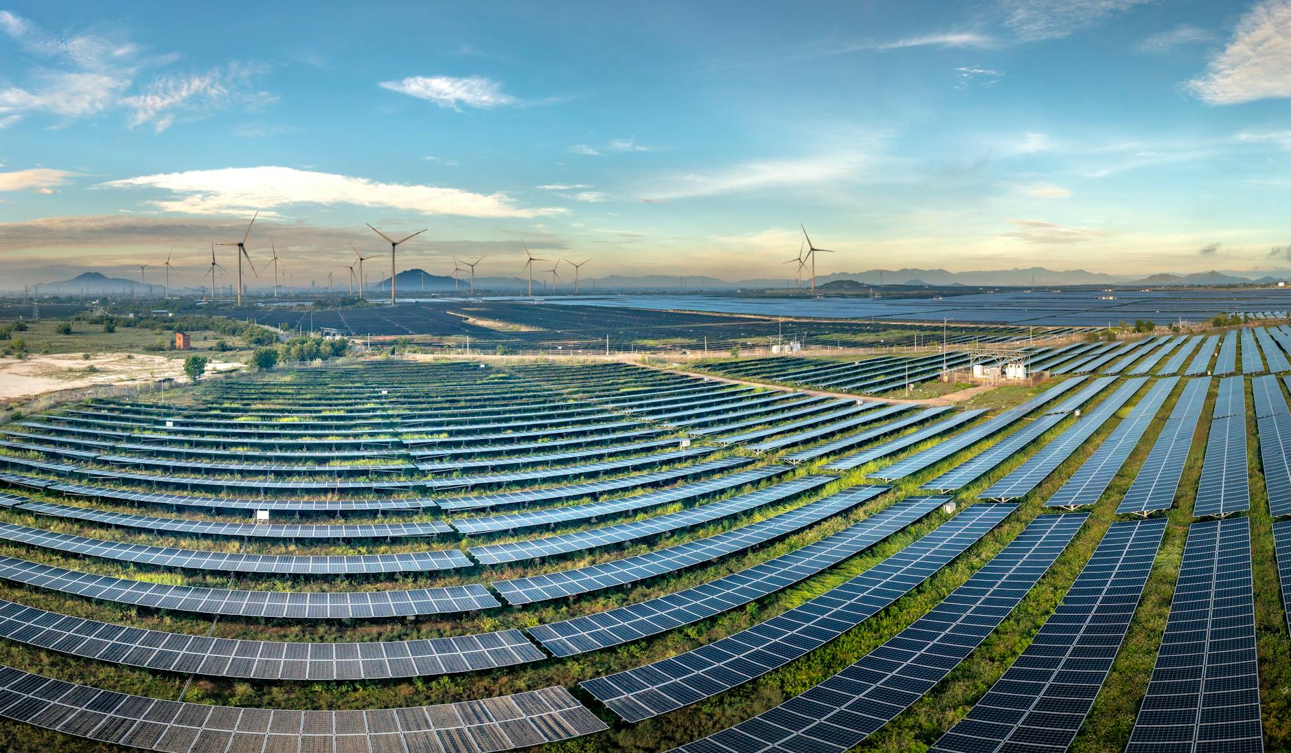 Landini contro accise — Expansive solar farm with wind turbines in the background under a clear blue sky.