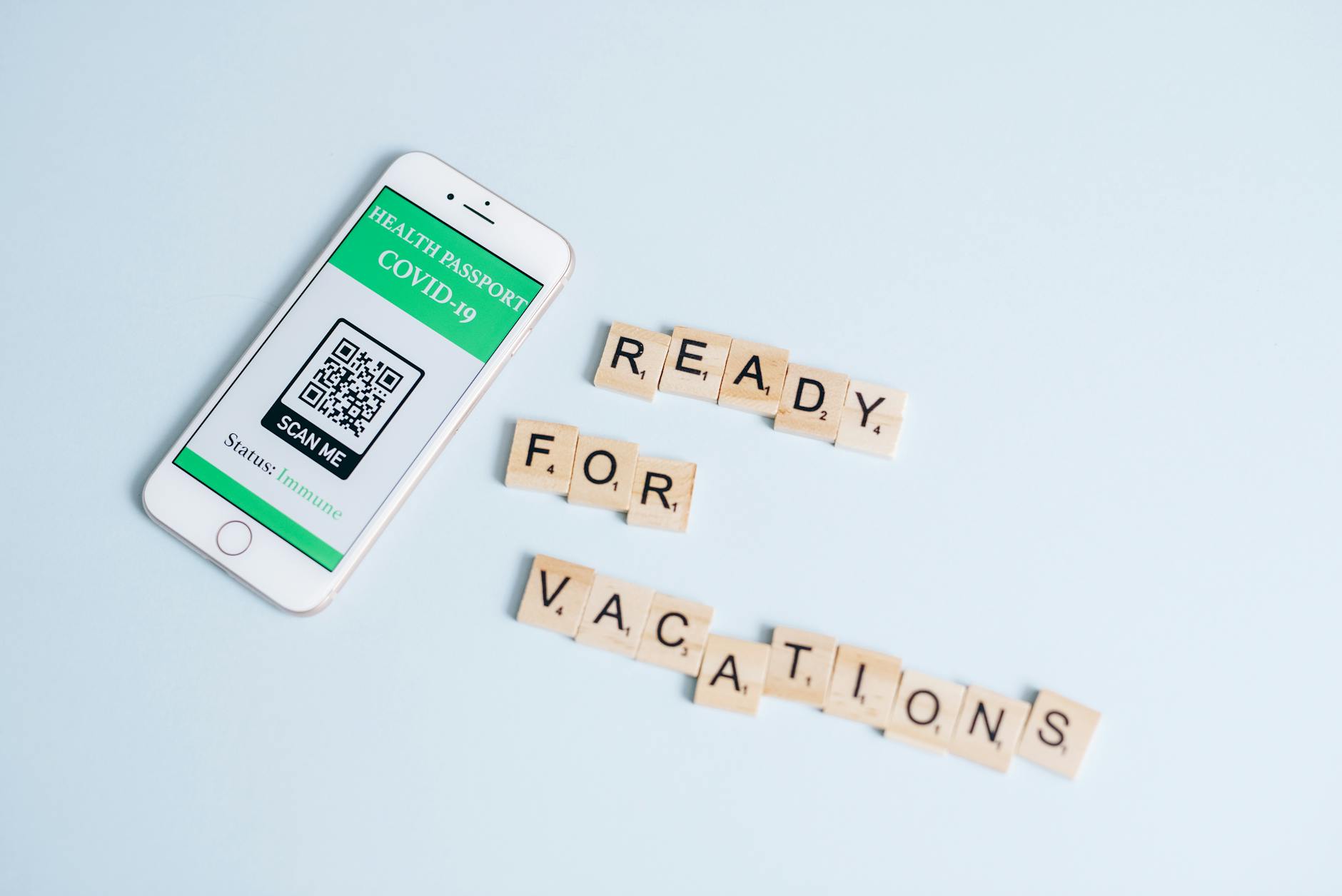 sostenibilità ambientale — Smartphone displaying COVID-19 health passport next to Scrabble letters spelling 'Ready for Vacations' on a pastel background.