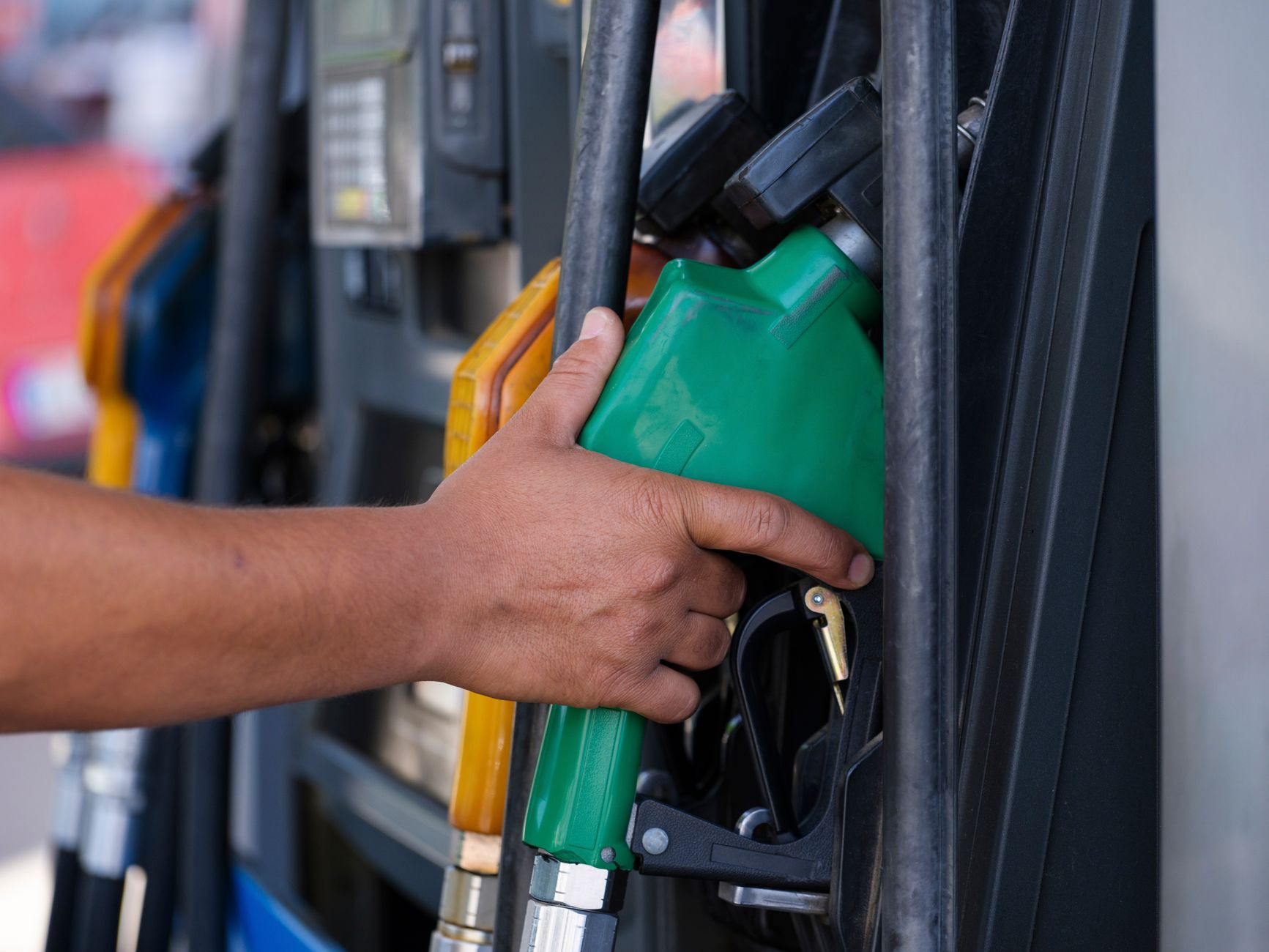 proroga accise carburanti — Close-up of a hand holding a green fuel nozzle at a gas pump station outdoors.