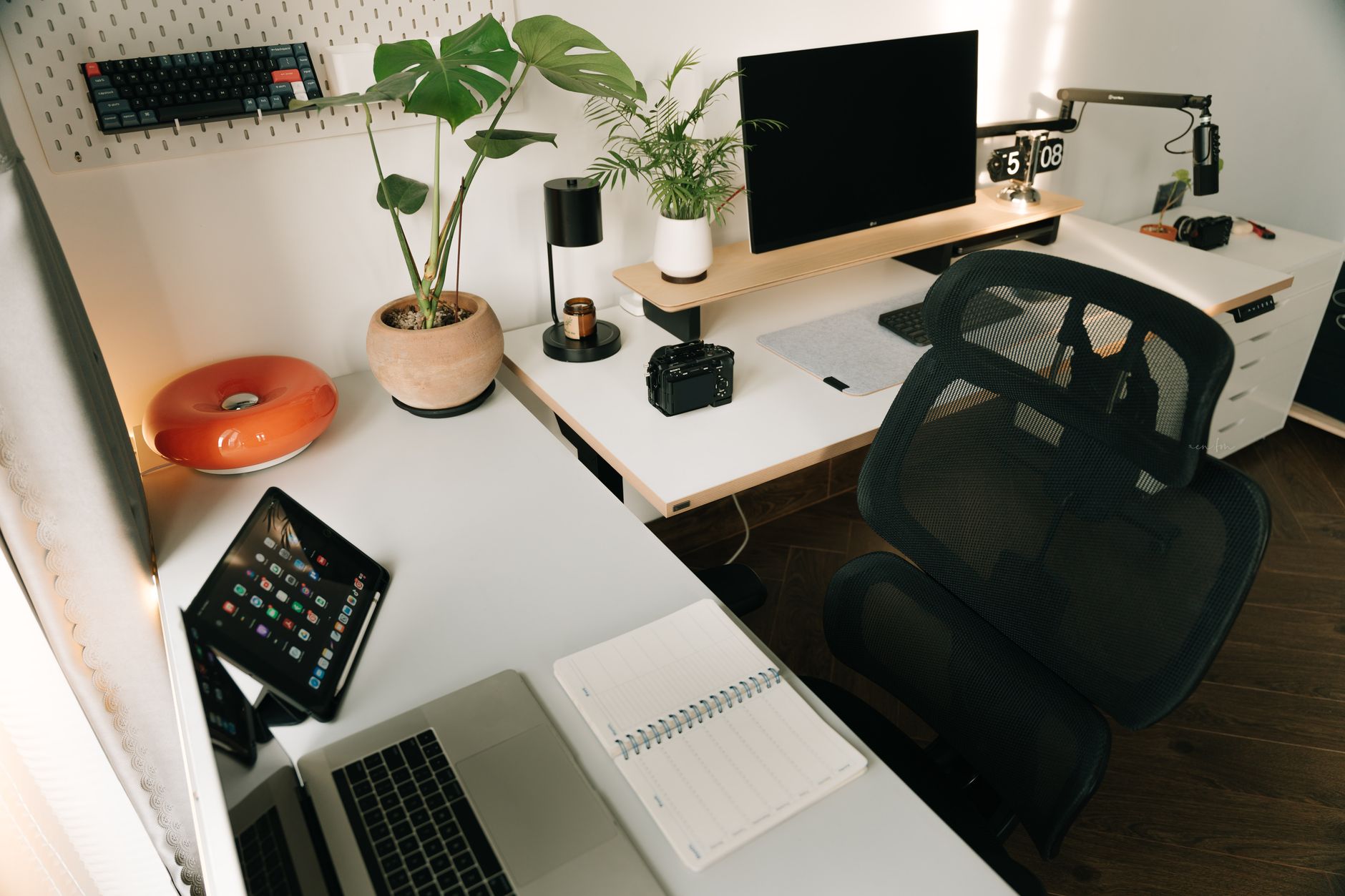 postazione lavoro domestico — A stylish home office setup featuring tech gadgets, a monitor, a tablet, and decorative plants in a minimalist design.