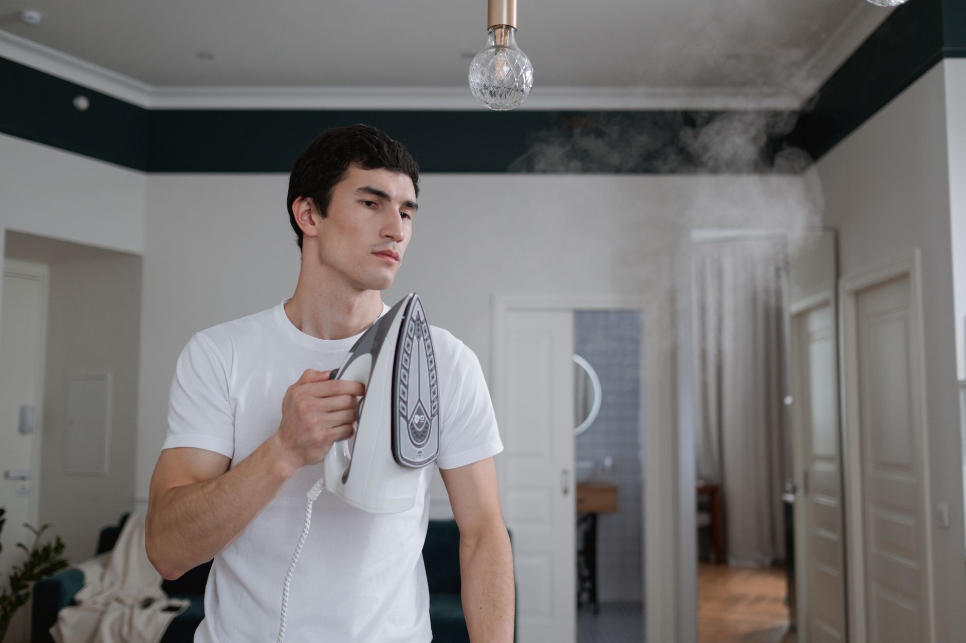 pulitori a vapore portatili — A man uses a steam iron on a white shirt indoors, highlighting daily household chores.