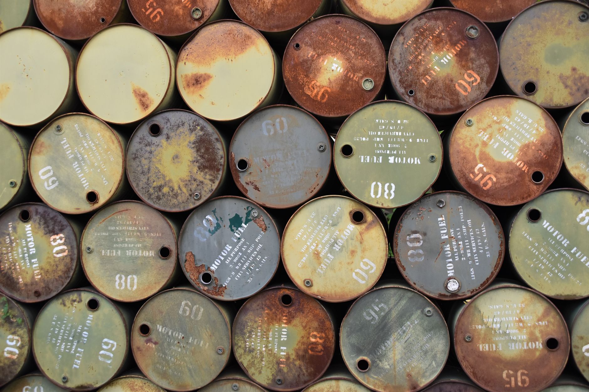 petrolio crolla — Pile of old, rusty oil barrels stacked outdoors with visible labels and numbers.