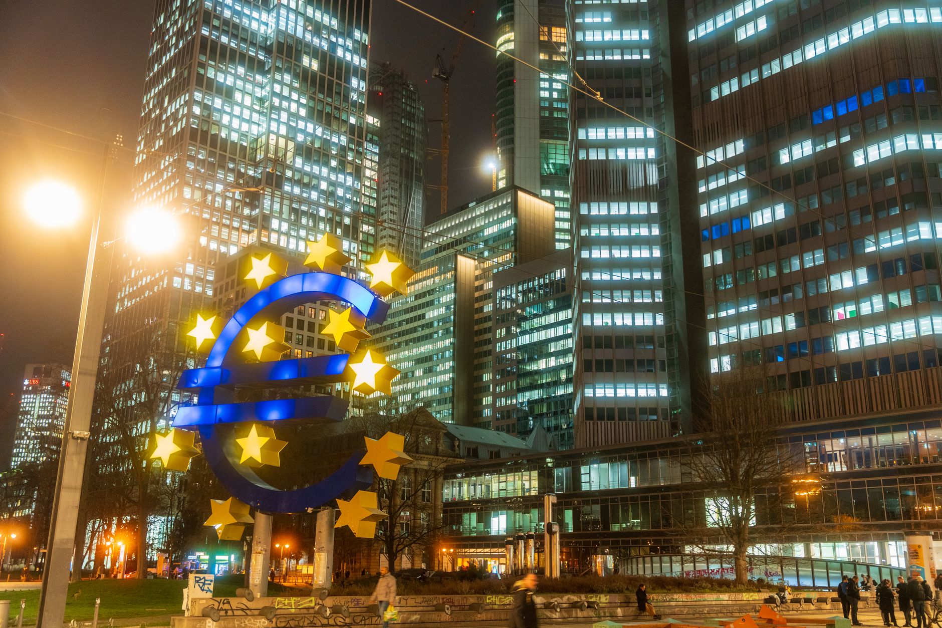 tassi BCE — Night view of the iconic Euro sculpture in Frankfurt's bustling financial district.