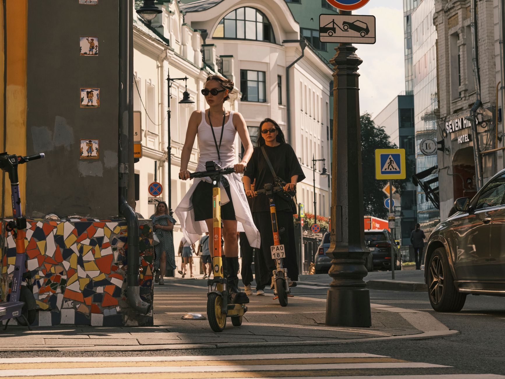 regole monopattini elettrici — Two women riding electric scooters on a city street, showcasing urban commute.