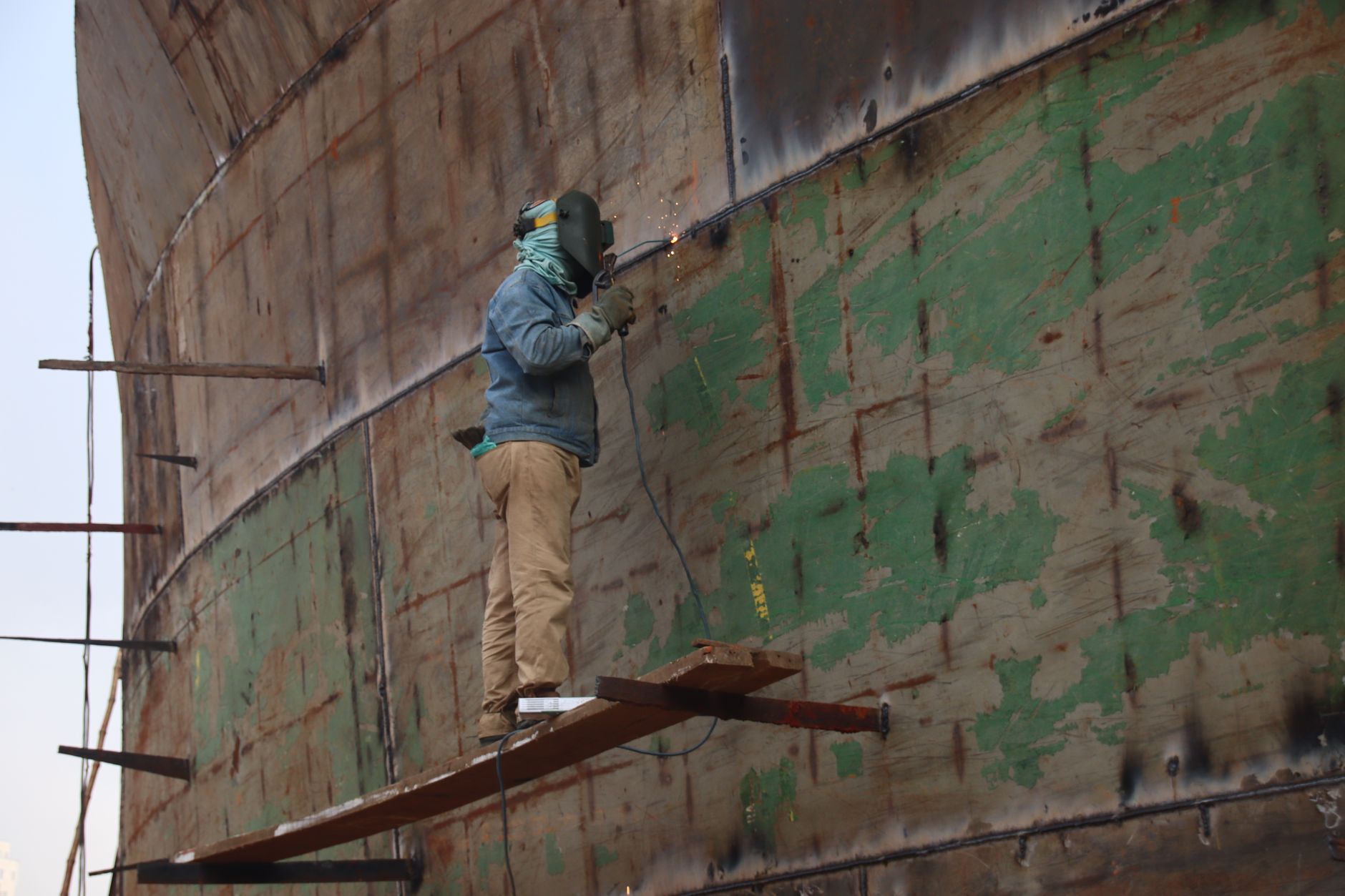 export credit navale — Worker welding a large ship's hull, outdoors, showcasing industrial craftsmanship.