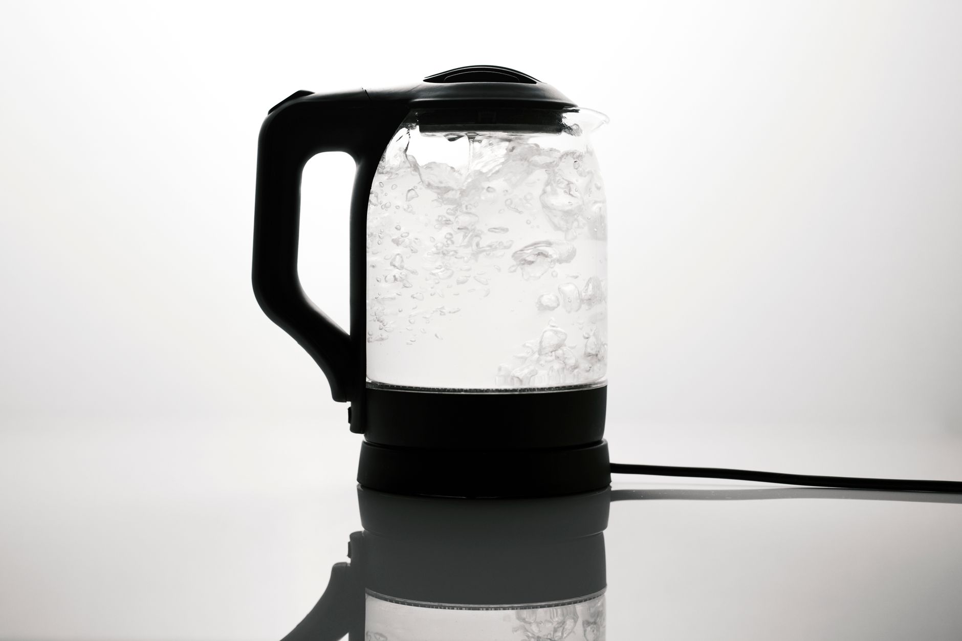 bollitori elettrici — A sleek electric kettle boiling water, captured on a reflective white surface.