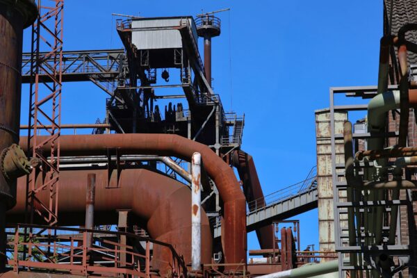 Detailed view of an industrial complex featuring rusted steel pipes and structures under a clear blue sky.