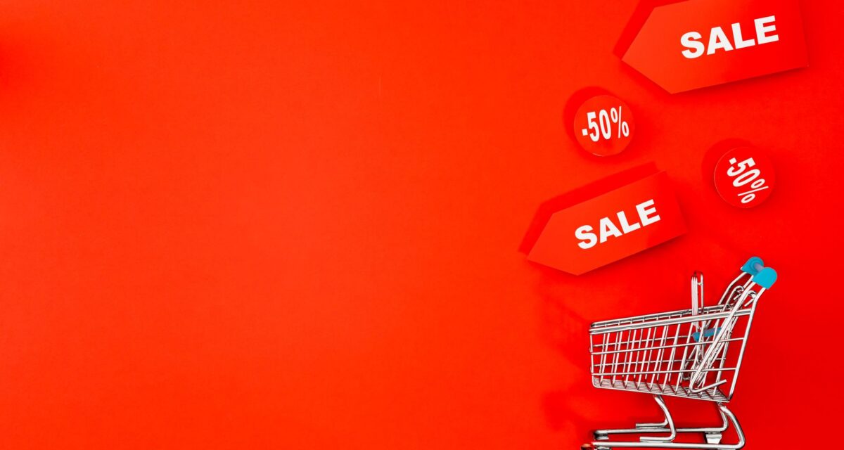 Shopping cart with sale tags on vibrant red backdrop promoting discounts.
