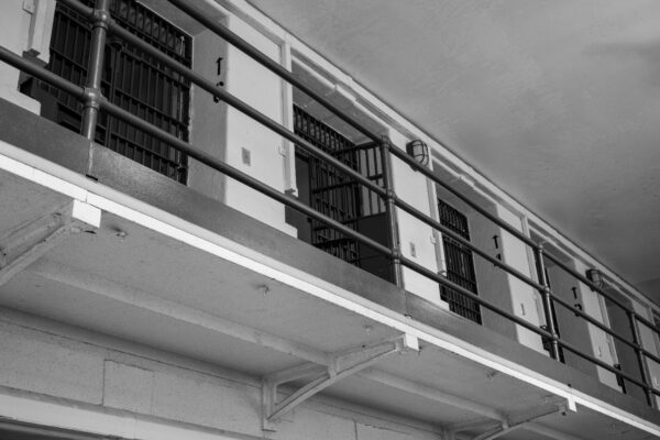 Monochrome view of prison cell block with barred doors and railing.
