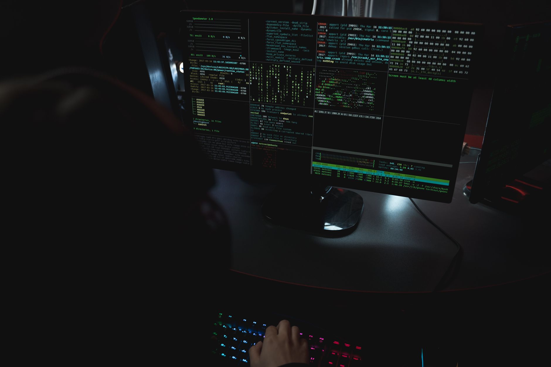 cyberattacchi rischio reale — Dark room setup with code displayed on PC monitors highlighting cybersecurity themes.