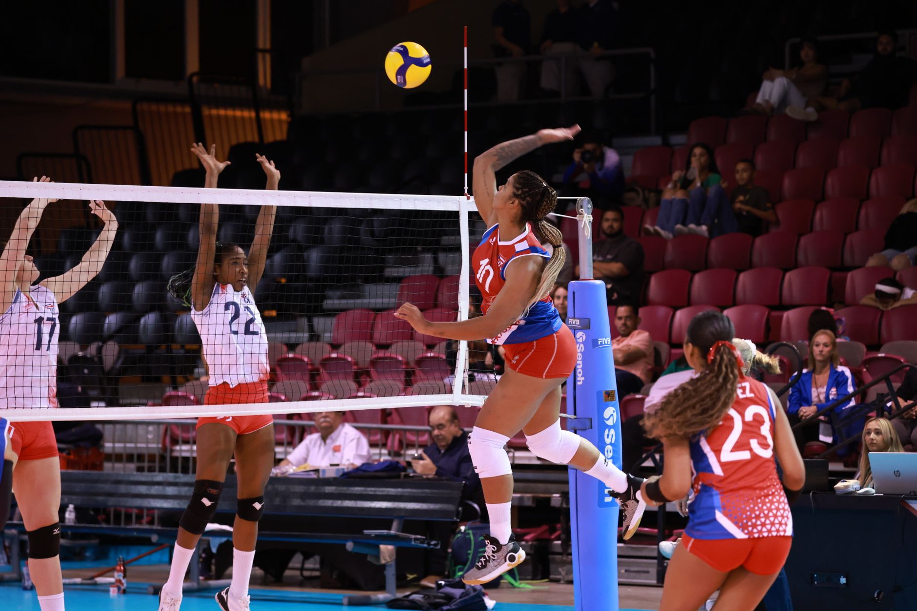 Dynamic action shot from a women's volleyball match with players in mid-air at the net.