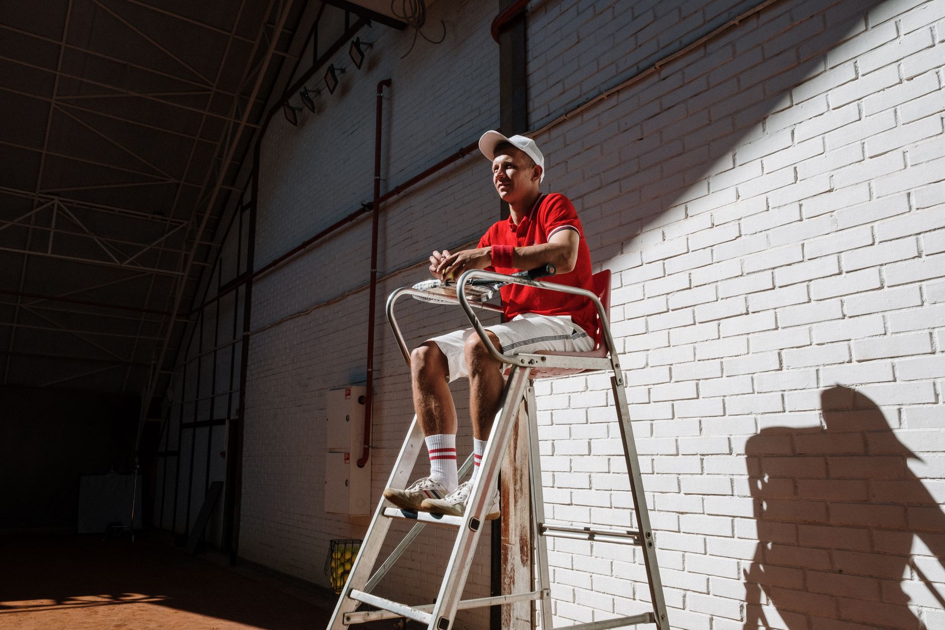Us Open odore di marijuana — Tennis umpire sitting on a high chair against a white brick wall, creating dynamic shadows indoors.
