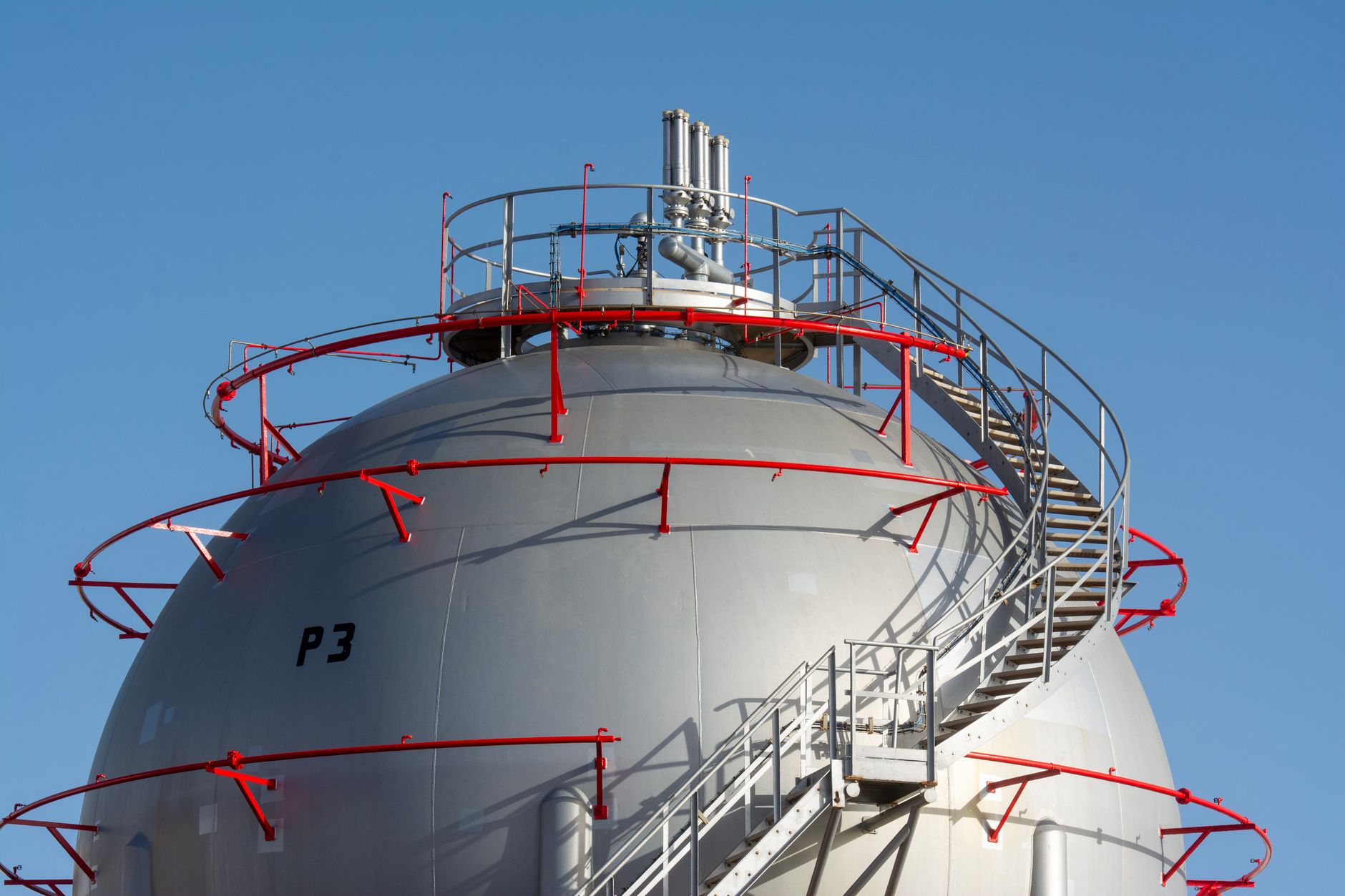 prezzo del gas — Close-up view of a large industrial gas storage sphere with a surrounding metal staircase.