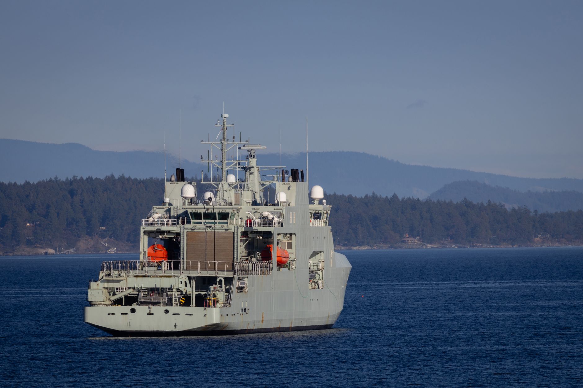 guerra Iran-Usa — A military warship navigates through open waters with a coastline backdrop on a clear day.