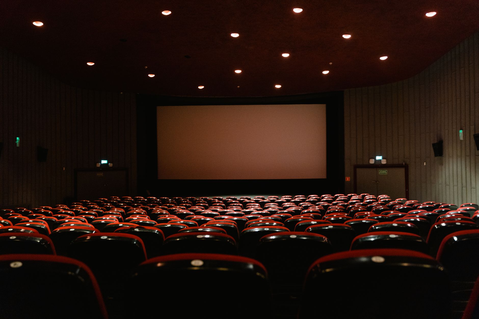 sale cinematografiche più belle d'Europa — A dimly lit empty cinema theater with rows of red chairs facing a projector screen.