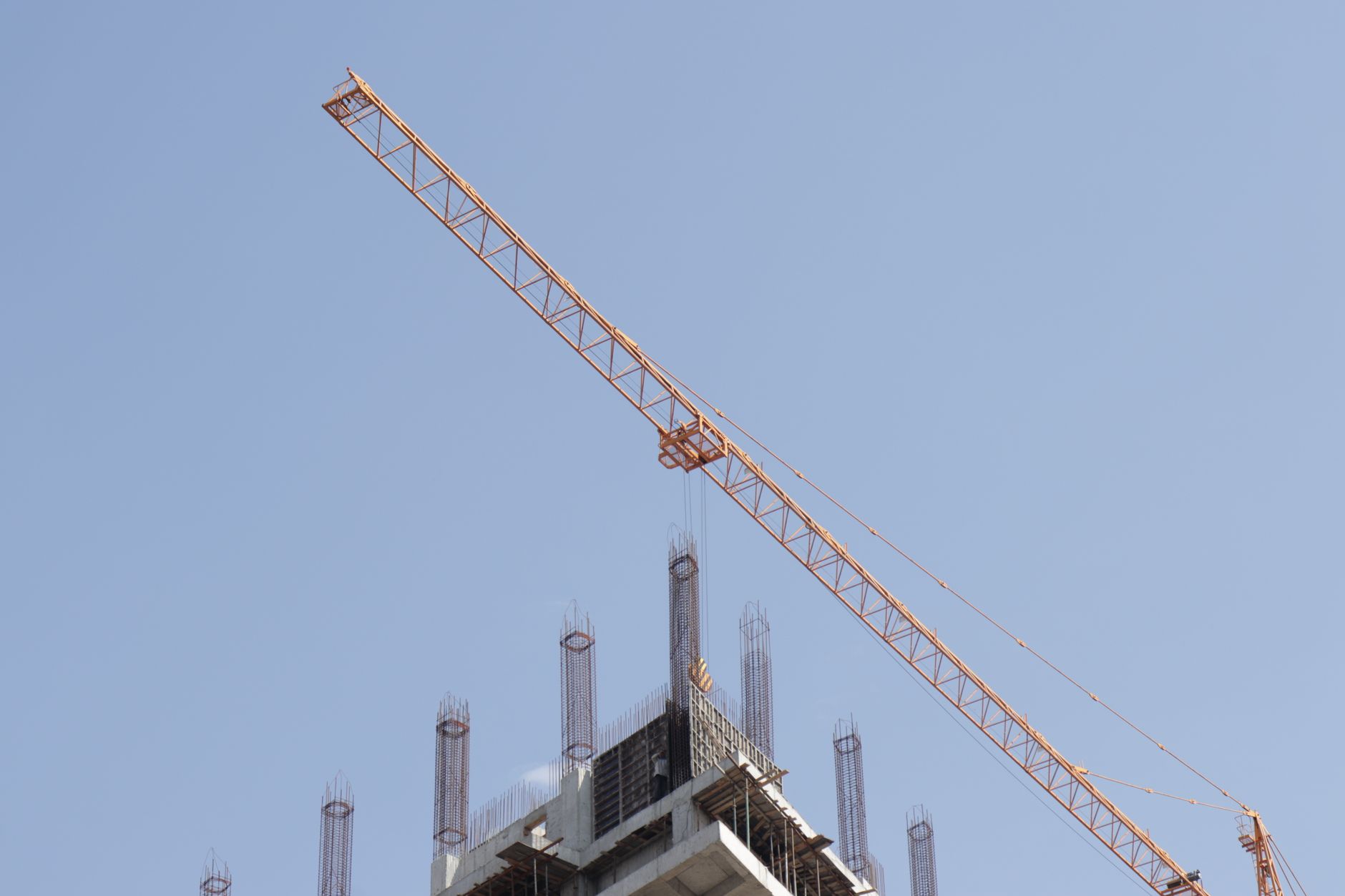 Tower crane working on a high-rise building construction site against a clear blue sky.