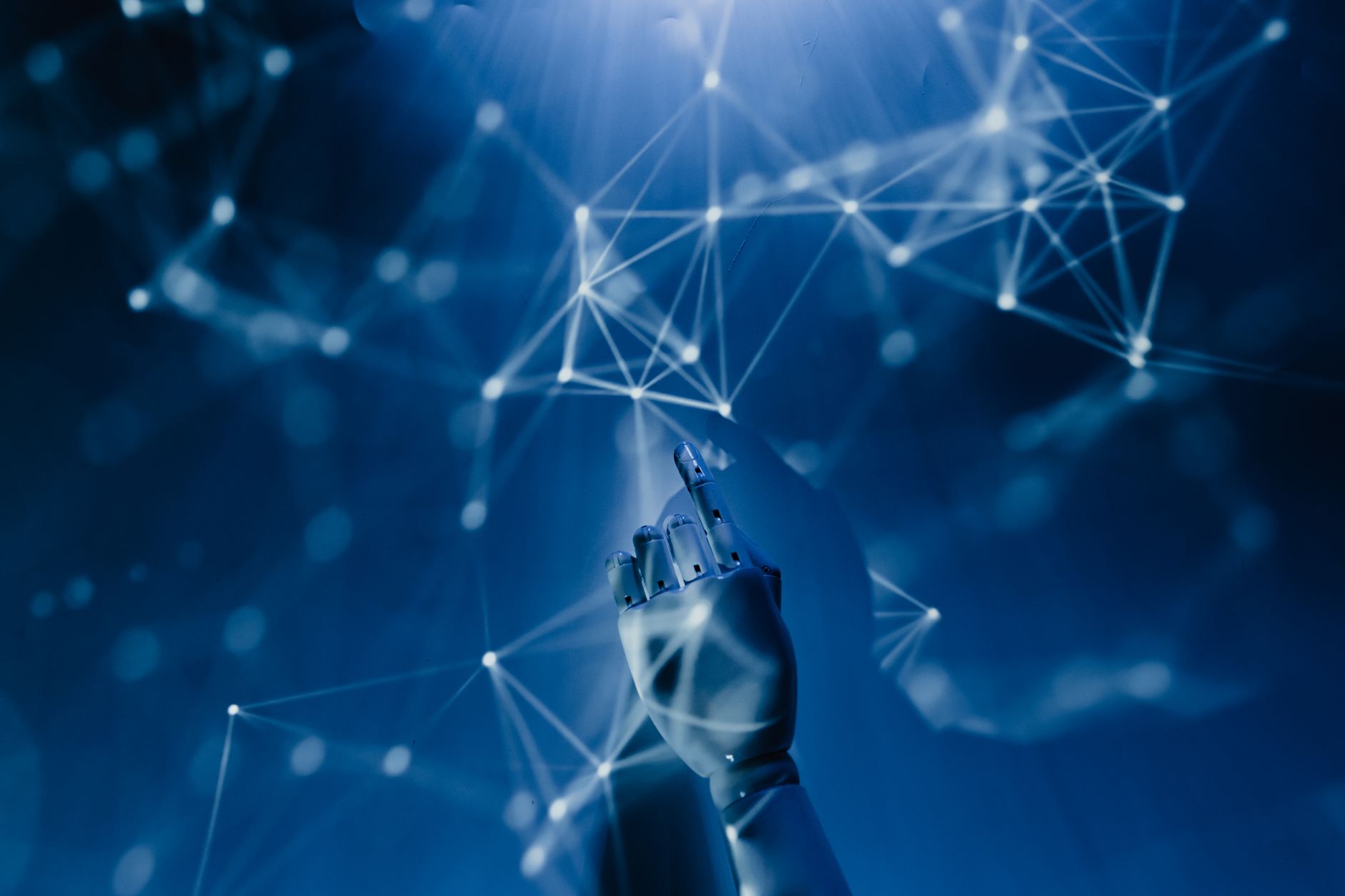 rischi dell'intelligenza artificiale — A robotic hand reaching into a digital network on a blue background, symbolizing AI technology.