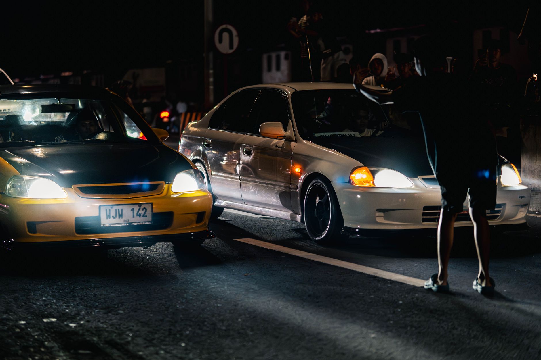 Dramatic night shot capturing street car racing with onlookers and vivid headlights.