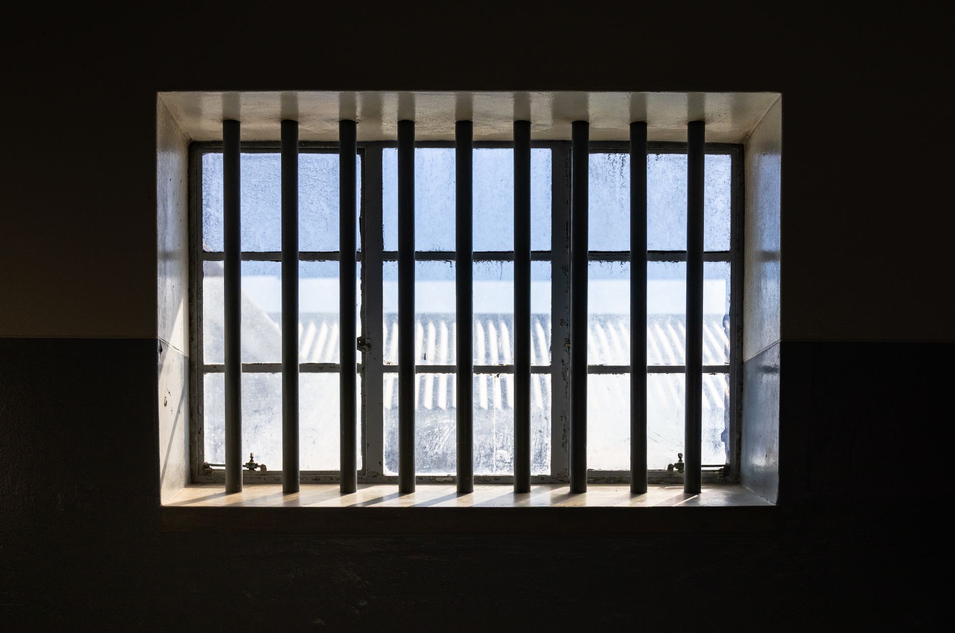 rivolta in carcere — Sunlight streams through barred window of a prison cell, casting shadows and light patterns.