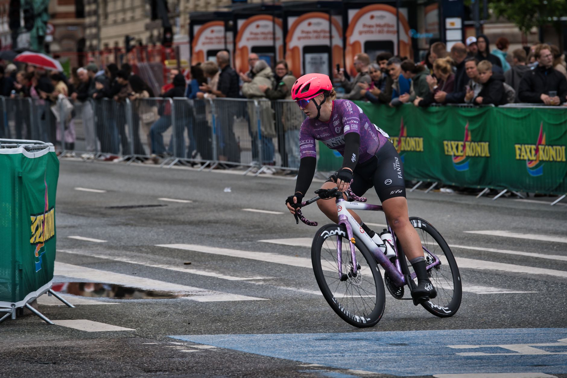 Mondiale di ciclismo in Trentino — Cyclist competes in urban race, navigating wet roads and city street as spectators watch.